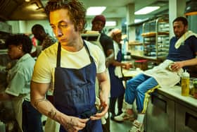 Jeremy Allen White as Carmen ‘Carmy’ Berzatto in The Bear, wearing a blue apron, holdin a spoon in a restaurant kitchen (Credit: Frank Ockenfels/FX )