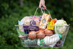 A woman holds a shopping basket of groceries.