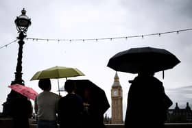 Pedestrian stand under umbrellas while looking at Elizabeth Tower, commonly called Big Ben from the Southbank by the River Thames, in central London, on July 31, 2023 on a gloomy and rainy summer day.