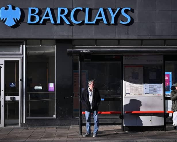 Commuters wait at a bus stop outside a branch of Barclays in London.