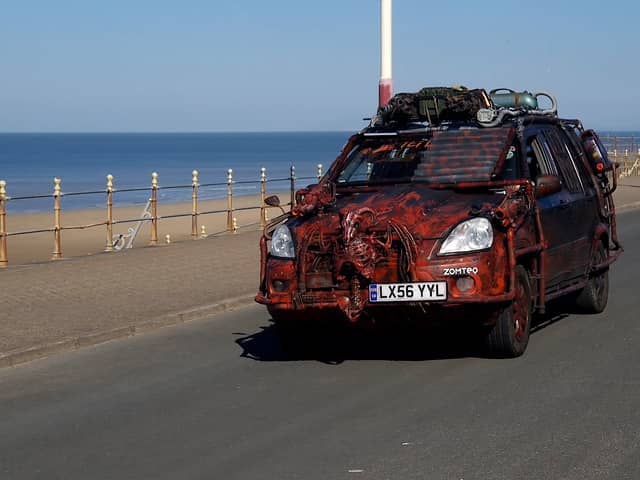 A zombie themed vehicle driving on a road by the coast
