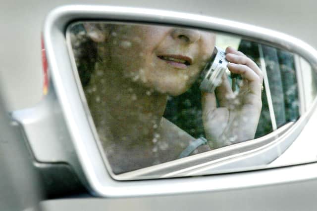 File photo:  A woman, reflected in a rear-view mirror, talks on a mobile phone while driving in traffic (Photo by Ian Waldie/Getty Images)