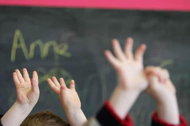 Children wave their hands in a classroom (Photo by Christopher Furlong/Getty Images).