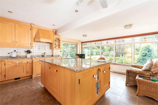 This room is fitted with custom-built maple wood units, including a central island with an inset sink, all with granite work surfaces. The breakfast area has sliding doors to the driveway