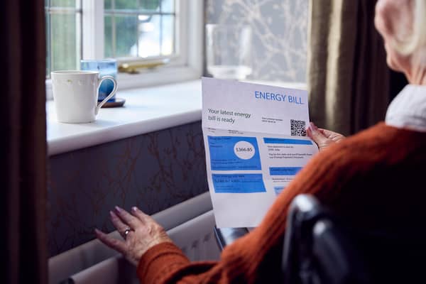 File photo of an elderly woman standing in front of a radiator holding an energy bill.
