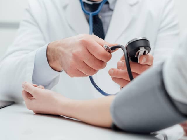 Doctor checking blood pressure of a patient, he is measuring pulses with a sphygmomanometer, hands close up